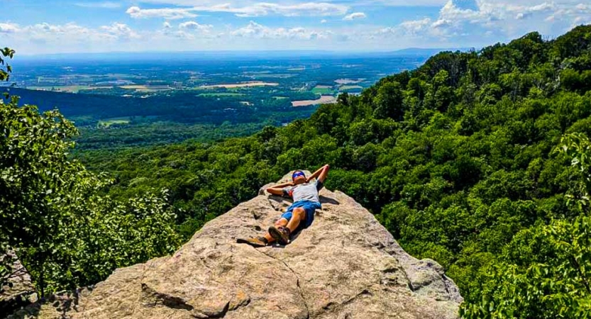 a student rests on a rock overlooking green forests on a backpacking trip for teens